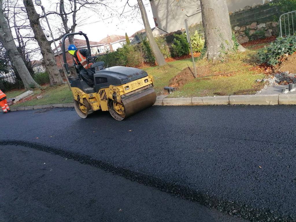 Yellow steamroller on a freshly paved road with driver